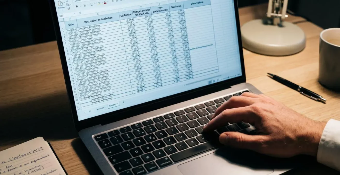 Écran d'ordinateur affichant un tableur de calcul financier avec colonnes CA facturé, Charges sociales et Salaire net en français, main tapant sur clavier